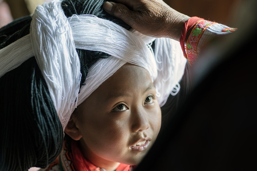 Gaoxing China 29 April 2026 View of a young Long Horn Miao girl wearing a traditional large headdress made of black and white yarn while an adult hand adjusts it. Gaoxing China 29 April 2026 View of a young Long Horn Miao girl wearing a traditional large headdress made of black and white yarn while an adult hand adjusts it.