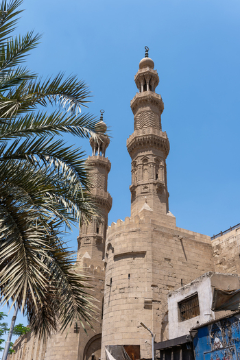 View of Bab Zuwayla with its two towering ornate minarets and palm tree fronds under a clear blue sky in El Darb El Ahmar Cairo Governorate Egypt. View of Bab Zuwayla with its two towering ornate minarets and palm tree fronds under a clear blue sky in El Darb El Ahmar Cairo Governorate Egypt.