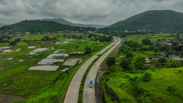 Aerial view of the Mumbai Goa Highway winding through lush green rice paddies and rolling hills under a cloudy sky in Mahad Maharashtra India.