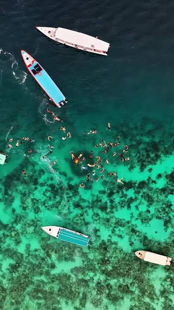 Aerial view of boats and swimmers in turquoise water Indonesia.