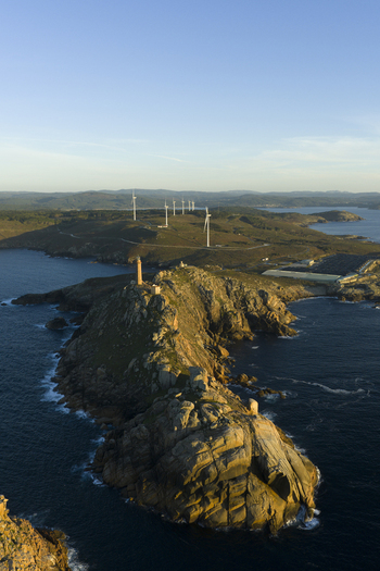 Aerial view of Cabo Vilan lighthouse on a rocky peninsula with wind turbines in the background in Galicia Spain.