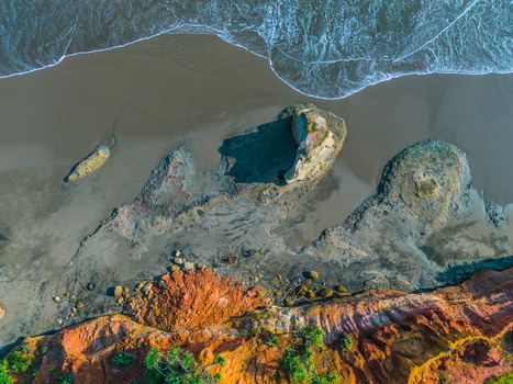 Aerial view of the rugged coastline with colorful cliffs dark sandy beach and crashing waves in Bali Bali Indonesia. Aerial view of the rugged coastline with colorful cliffs dark sandy beach and crashing waves in Bali Bali Indonesia.