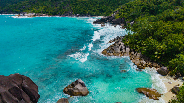 Aerial view of Anse Soleil Beachcomber Hotel nestled among lush tropical greenery and granite boulders along the turquoise coastline of Mahe Baie Lazare Seychelles.