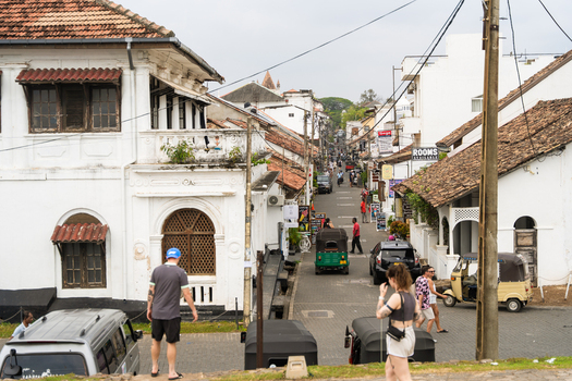 Galle Sri Lanka 07 January 2026 View of historic colonial buildings with terracotta roofs and a green tuk tuk on a narrow street with people walking in Galle Fort.