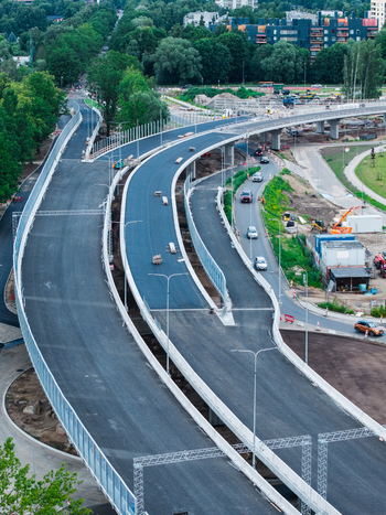 Aerial view of a new road construction project with curved asphalt lanes concrete barriers and surrounding green trees in Riga Latvia. Aerial view of a new road construction project with curved asphalt lanes concrete barriers and surrounding green trees in Riga Latvia.