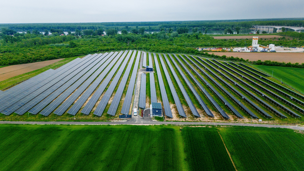 Aerial view of a large solar panel farm surrounded by lush green agricultural fields and dense forests near a river in Sabac Vojvodina Serbia.