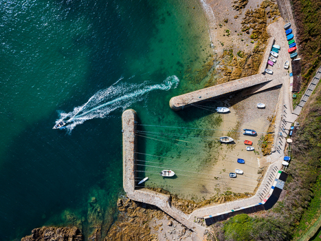 Aerial view of Port Racine with small boats moored in the harbor and a motorboat leaving the breakwater in La Hague Normandie France.
