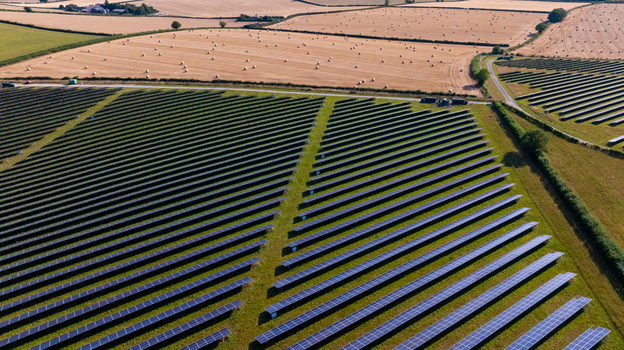 Aerial view of a large solar farm with rows of photovoltaic panels set in a rural landscape with harvested fields and hay bales in Dorset England United Kingdom.