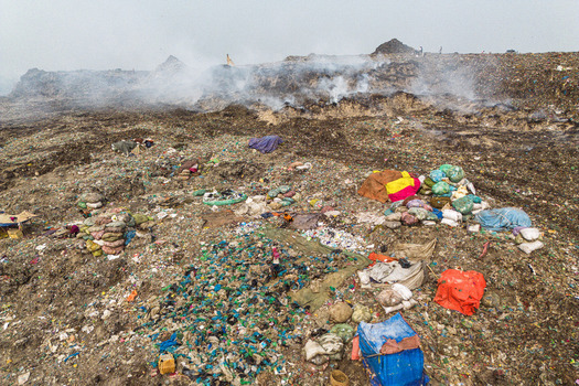 Aminbazar Bangladesh 26 January 2025 Aerial view of the Aminbazar landfill with smoke rising from waste piles and waste pickers working among colorful bags under a hazy sky. Aminbazar Bangladesh 26 January 2025 Aerial view of the Aminbazar landfill with smoke rising from waste piles and waste pickers working among colorful bags under a hazy sky.