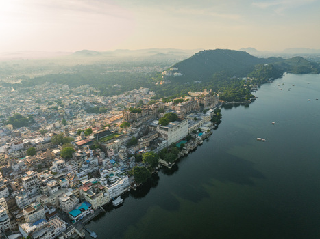 Aerial view of the historic City Palace complex situated on the banks of Lake Pichola with surrounding urban architecture and hills in Udaipur Rajasthan India.