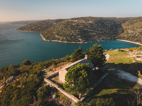 Aerial view of a quaint chapel perched atop a hill overlooking the shimmering Adriatic framed by rugged coastline and verdant hillsides Rakalj Istria County Croatia.