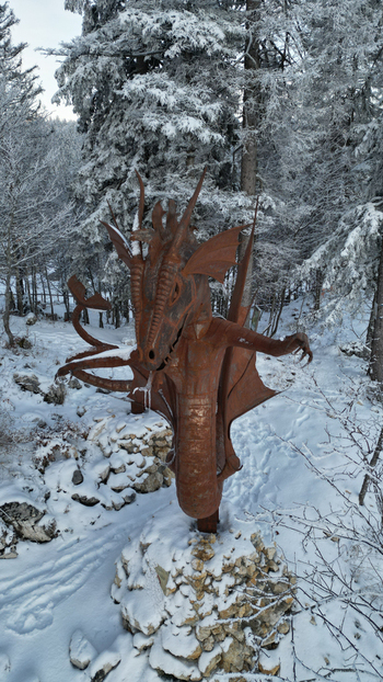 View of a metal dragon sculpture standing in a snowy forest at Col de la Faucille Gex Auvergne Rhone Alpes France. View of a metal dragon sculpture standing in a snowy forest at Col de la Faucille Gex Auvergne Rhone Alpes France.
