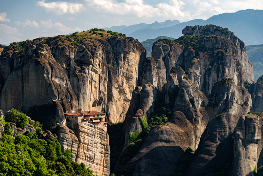 Aerial view of Meteora monastery perched on towering sandstone rock formations surrounded by lush green trees and dramatic cliffs under a bright blue sky in Trikala Greece. Aerial view of Meteora monastery perched on towering sandstone rock formations surrounded by lush green trees and dramatic cliffs under a bright blue sky in Trikala Greece.