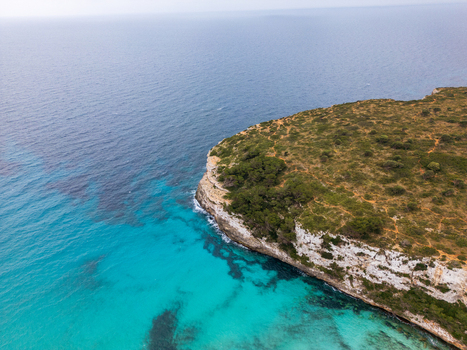 Aerial view of the rugged limestone cliffs and crystal clear turquoise waters along the Mediterranean coast Cala Mendia Illes Balears Spain. Aerial view of the rugged limestone cliffs and crystal clear turquoise waters along the Mediterranean coast Cala Mendia Illes Balears Spain.