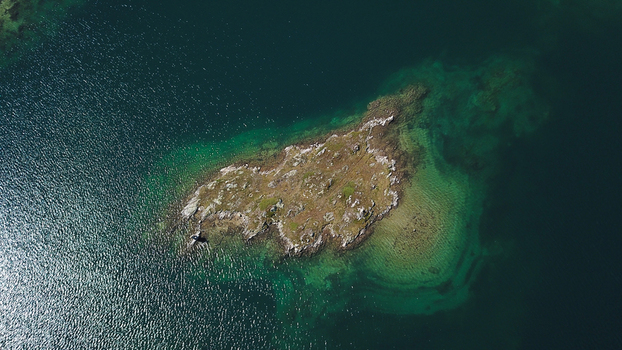 Aerial view of a small rocky island surrounded by turquoise alpine water and sunlight reflections in Obergoms Valais Switzerland. Aerial view of a small rocky island surrounded by turquoise alpine water and sunlight reflections in Obergoms Valais Switzerland.
