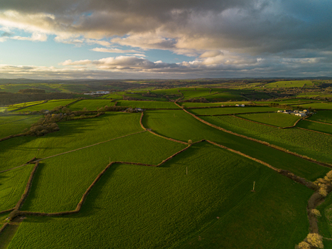 Aerial view of lush green rolling fields divided by traditional stone walls and hedgerows under a dramatic sunset sky in the countryside of Looe Cornwall United Kingdom. Aerial view of lush green rolling fields divided by traditional stone walls and hedgerows under a dramatic sunset sky in the countryside of Looe Cornwall United Kingdom.