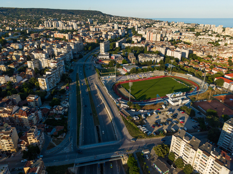 Varna Bulgaria 23 June 2026 Aerial view of Spartak Stadium surrounded by urban residential buildings a multi lane road and green trees under a clear sky.
