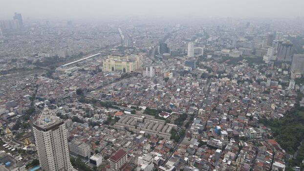 Aerial view of the dense urban landscape of Jakarta Pusat featuring high rise buildings and residential rooftops under a hazy sky in Kecamatan Menteng Daerah Khusus Ibukota Indonesia. Aerial view of the dense urban landscape of Jakarta Pusat featuring high rise buildings and residential rooftops under a hazy sky in Kecamatan Menteng Daerah Khusus Ibukota Indonesia.