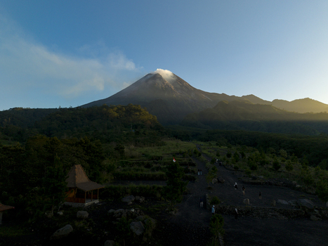 Aerial view of Bunker Kaliadem Merapi with the smoking peak of Mount Merapi surrounded by lush green forests under a clear blue sky Kecamatan Pakem Daerah Istimewa Yogya Indonesia. Aerial view of Bunker Kaliadem Merapi with the smoking peak of Mount Merapi surrounded by lush green forests under a clear blue sky Kecamatan Pakem Daerah Istimewa Yogya Indonesia.