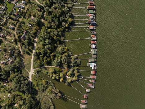 Aerial view of Bokodi Floating Village with colorful wooden houses on stilts over the lake surrounded by lush trees and green water in Oroszlany Hungary. Aerial view of Bokodi Floating Village with colorful wooden houses on stilts over the lake surrounded by lush trees and green water in Oroszlany Hungary.
