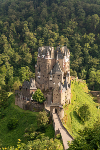 View of Eltz Castle featuring its medieval stone architecture and pointed turrets nestled within a dense green forest in Wierschem Rhineland Palatinate Germany. View of Eltz Castle featuring its medieval stone architecture and pointed turrets nestled within a dense green forest in Wierschem Rhineland Palatinate Germany.