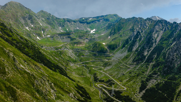 Aerial view of the winding Transfagarasan road snaking through lush green Fagaras Mountains with rocky peaks and patches of snow in Curtea de Arges Judetul Arges Romania.