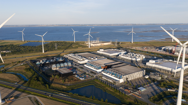 Aerial view of a large data center complex surrounded by wind turbines and green fields near the coast in Eemshaven Groningen Netherlands.