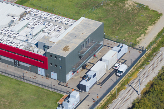 Aerial view of a modern datacenter facility featuring industrial cooling units on the roof a red accent wall and service vehicles parked in the compound in Arezzo Tuscany Italy. Aerial view of a modern datacenter facility featuring industrial cooling units on the roof a red accent wall and service vehicles parked in the compound in Arezzo Tuscany Italy.