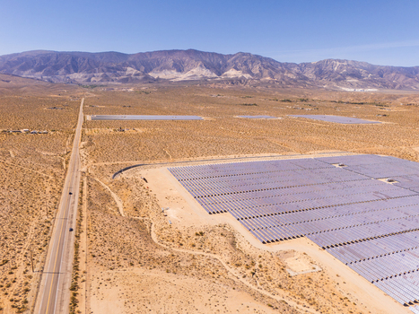 Aerial view of a large solar farm with rows of photovoltaic panels in the desert landscape near a straight road and mountains in Lucerne Valley California United States. Aerial view of a large solar farm with rows of photovoltaic panels in the desert landscape near a straight road and mountains in Lucerne Valley California United States.