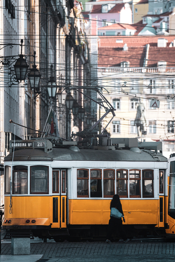 View of a classic yellow tram 28 passing through a city street with overhead wires and historic architecture near Praca do Comercio Lisbon Lisbon Portugal.