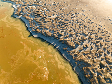Aerial view of the rugged textured volcanic landscape meeting the mineral rich yellowish geothermal waters of the Reykjanes Peninsula Reykjanesbaer Iceland. Aerial view of the rugged textured volcanic landscape meeting the mineral rich yellowish geothermal waters of the Reykjanes Peninsula Reykjanesbaer Iceland.
