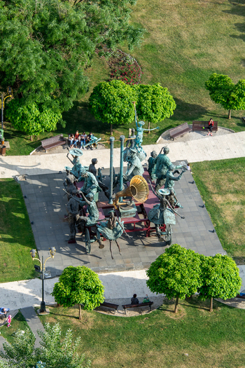 View of a bronze sculpture group featuring musicians and dancers with a gramophone in a park with green trees and paved paths in Bucharest Bucharest Romania. View of a bronze sculpture group featuring musicians and dancers with a gramophone in a park with green trees and paved paths in Bucharest Bucharest Romania.