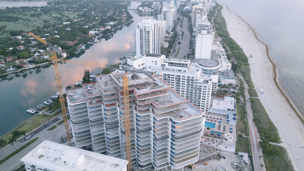 Aerial view of a high rise building under construction with tower cranes situated between the waterway and the sandy beach in Miami Beach Florida United States. Aerial view of a high rise building under construction with tower cranes situated between the waterway and the sandy beach in Miami Beach Florida United States.
