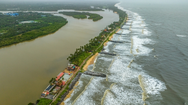 Aerial view of Mattu Beach featuring a narrow strip of land separating the backwaters from the Arabian Sea with rocky breakwaters and palm trees in Udupi Karnataka India.