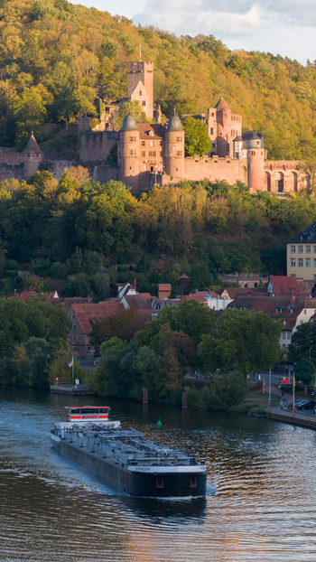 Aerial view of Wertheim Castle perched on a forested hill overlooking the river with a cargo ship navigating the waterway in Wertheim Baden Wurttemberg Germany.