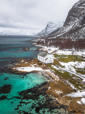 Aerial view of the Gimsøy Church a beacon of white against the turquoise waters and snow dusted landscape stands majestically Gimsøysand Nordland Norway. Aerial view of the Gimsøy Church a beacon of white against the turquoise waters and snow dusted landscape stands majestically Gimsøysand Nordland Norway.