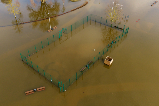 Aerial view of a flooded sports court with green fencing and submerged benches surrounded by murky water and bare trees in Kedainiai Kaunas County Lithuania. Aerial view of a flooded sports court with green fencing and submerged benches surrounded by murky water and bare trees in Kedainiai Kaunas County Lithuania.