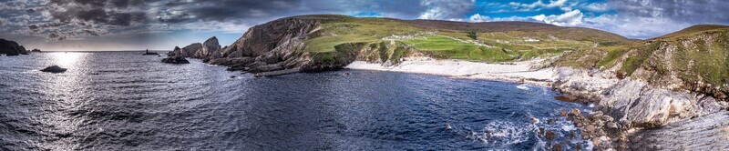 Aerial view of An Port featuring rugged cliffs a secluded beach and green hills along the Atlantic coastline in Ardara County Donegal Ireland.