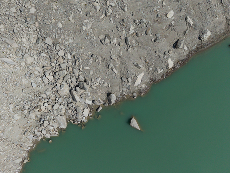 Aerial view of the rocky shoreline at Gelmersee reservoir showing low water levels and turquoise alpine water Switzerland.