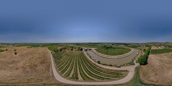 Aerial view of the Canal du Midi winding through lush vineyards near Le Chat Qui Peche with a stone bridge and rural landscape in Argeliers Occitanie France.