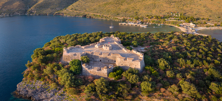 Aerial view of the historic Porto Palermo Castle a triangular stone fortress on a green peninsula overlooking the blue waters of the Ionian Sea in Porto Palermo Qarku i Vlores Albania. Aerial view of the historic Porto Palermo Castle a triangular stone fortress on a green peninsula overlooking the blue waters of the Ionian Sea in Porto Palermo Qarku i Vlores Albania.
