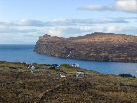 Aerial view of the coastal village of Milovaig with houses overlooking the blue waters of Loch Pooltiel and dramatic cliffs on the Isle of Skye Milovaig Scotland United Kingdom.