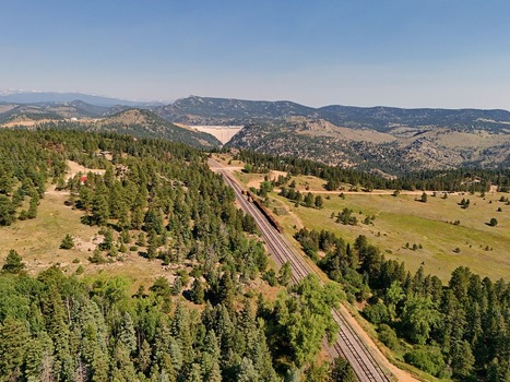 Aerial view of a freight train traveling along railway tracks through a dense pine forest in the mountainous landscape of Golden Colorado United States. Aerial view of a freight train traveling along railway tracks through a dense pine forest in the mountainous landscape of Golden Colorado United States.