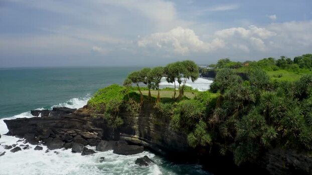 Aerial view of Tanah Lot temple area with rocky cliffs and waves Indonesia.