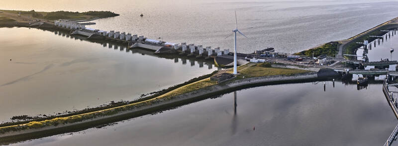 Den Oever Netherlands 19 June 2026 Aerial view of Stevinsluizen with sluice dams swing bridges and a wind turbine in early morning light. Den Oever Netherlands 19 June 2026 Aerial view of Stevinsluizen with sluice dams swing bridges and a wind turbine in early morning light.