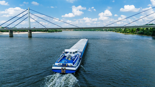 Aerial view of a large cargo barge navigating the Danube river towards the Liberty Bridge under a blue sky with white clouds in Novi Sad Vojvodina Serbia. Aerial view of a large cargo barge navigating the Danube river towards the Liberty Bridge under a blue sky with white clouds in Novi Sad Vojvodina Serbia.