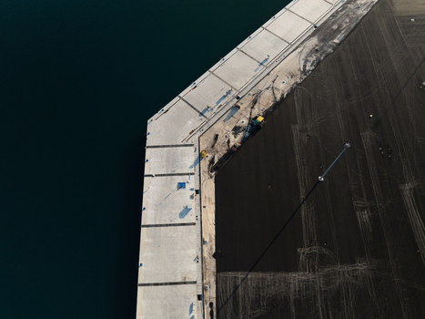 Aerial view of a concrete pier under construction with tire tracks on the dark ground and deep blue water in Augusta Sicily Italy. Aerial view of a concrete pier under construction with tire tracks on the dark ground and deep blue water in Augusta Sicily Italy.