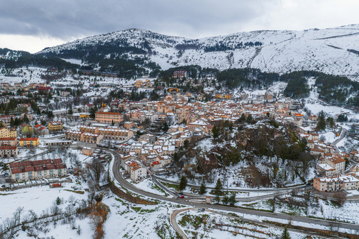 Aerial view of the historic village of Pescocostanzo nestled in snow covered mountains featuring traditional stone buildings and winding roads in Pescocostanzo Abruzzo Italy.