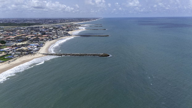 Aerial view of Lekki Beach Road area with stone breakwaters along the sandy coastline and urban buildings under a cloudy sky Lekki Lagos Nigeria. Aerial view of Lekki Beach Road area with stone breakwaters along the sandy coastline and urban buildings under a cloudy sky Lekki Lagos Nigeria.