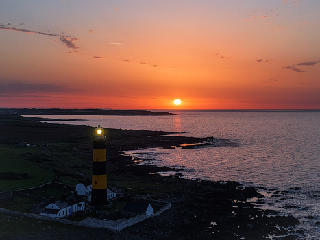 Aerial view of St. John s Point Lighthouse illuminated at sunset with rocky coastline and calm sea in Newcastle Northern Ireland United Kingdom. Aerial view of St. John s Point Lighthouse illuminated at sunset with rocky coastline and calm sea in Newcastle Northern Ireland United Kingdom.